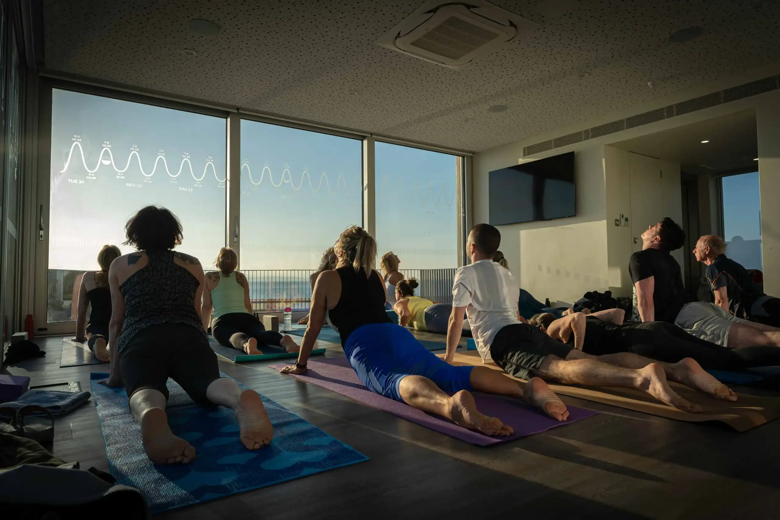 Yoga class in a bright, modern studio with participants stretching on mats during a relaxing session.